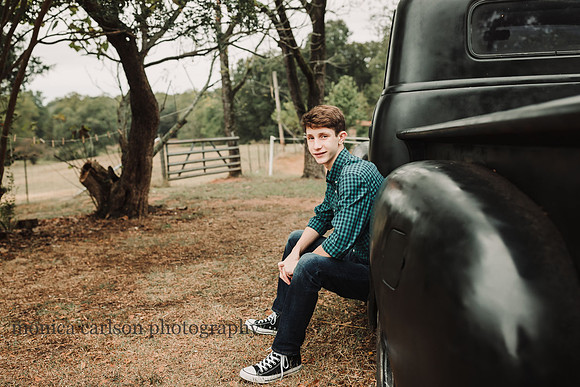 teenage boy sitting on the tire well of a old black truck on a farm
