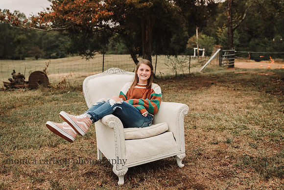 teen girl sitting in a white love seat with a farm field in the back ground