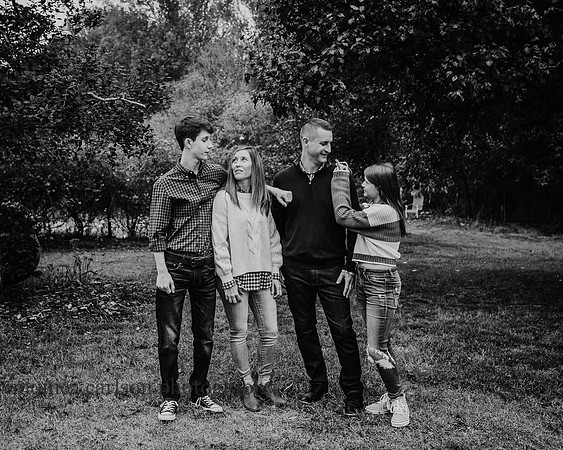 black and white image of a family of four laughing together on a farm by monica carlson