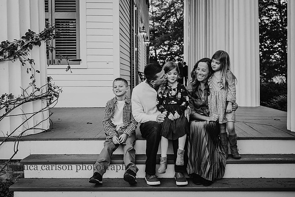 Father giving his daughter a kiss on the cheek while family watches outside a historic home in Roswell