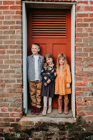 Three siblings stand in front of the red door of a ice house at Barrington hall