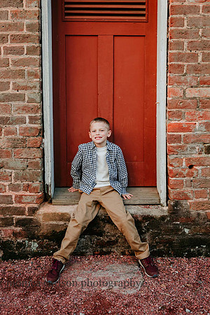 young boy sitting in front of a red door on the property of Barrington Hall