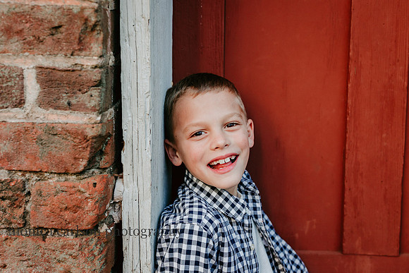 Portrait of a young boy in front of a red door taken by Monica Carlson