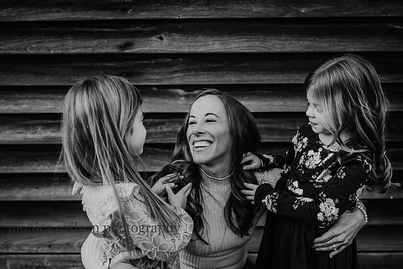 black and white portrait of a smiling mom with her daughters who are playing with her hair by monica carlson