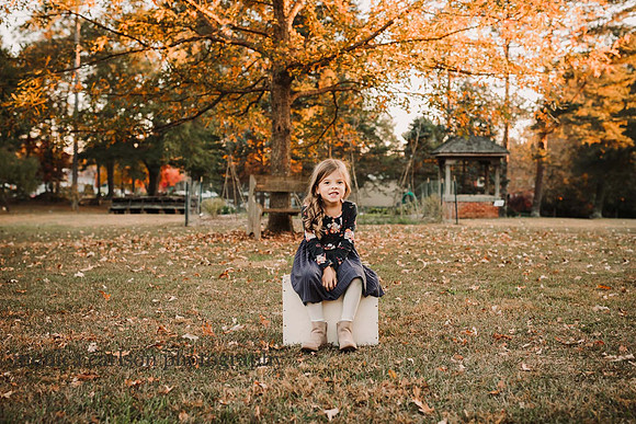 cute little girl sitting on a box with beautiful fall foliage behind her in Roswell, Georgia