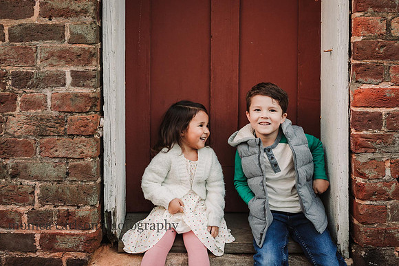siblings sharing a chuckle in front of a red door