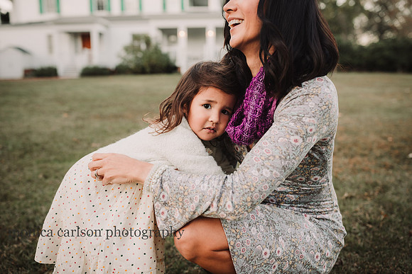 little girl holding on to her mother while mom laughs taken by monica carlson