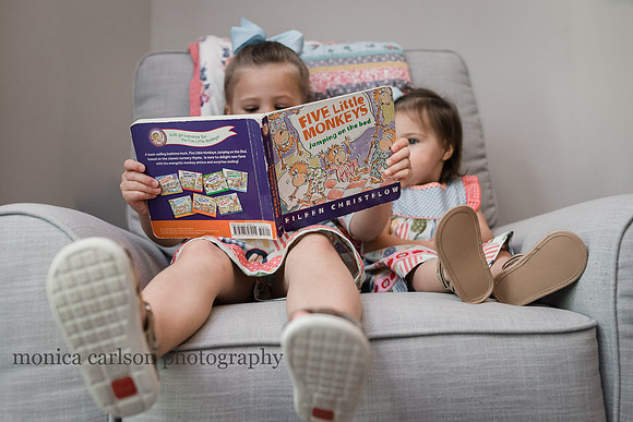 two little girls share a chair and read a book during a home photo session