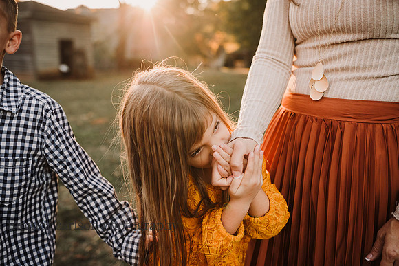 little girl lovingly kisses her mothers hand on a sunny day during a photo session with monica carlson