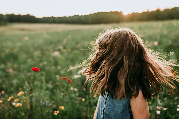 brunette girls golden hair waving in the wind on a wildflower field