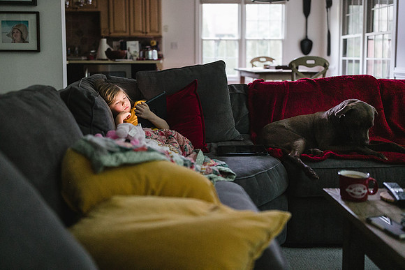 dog and a girl laying on a couch, looking at her ipad
