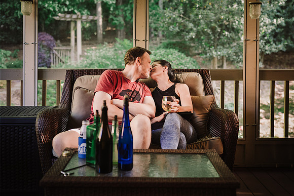 husband and wife sharing a kiss on a patio over a glass of wine and beer
