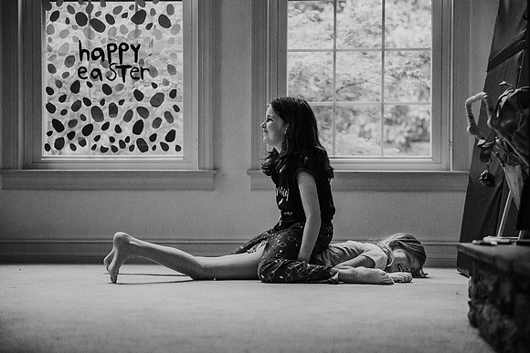 older sister sitting on her younger sister, both girls are laughing by monica carlson