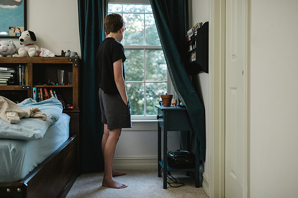 boy looking out the window of his room after just getting up