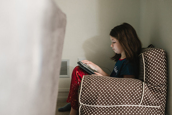 girl does her quarantine school work on a ipad while in her pajamas