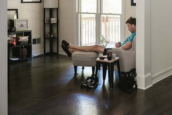 man doing his work during quarantine from home in his slippers and sitting in small love seat