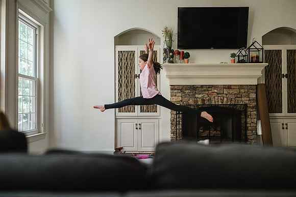 girl leaping over a couch during a quarantined gymnastics practice