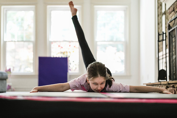 girl laying on her stomach on a gymnastics mat while kicking her leg above her head behind her
