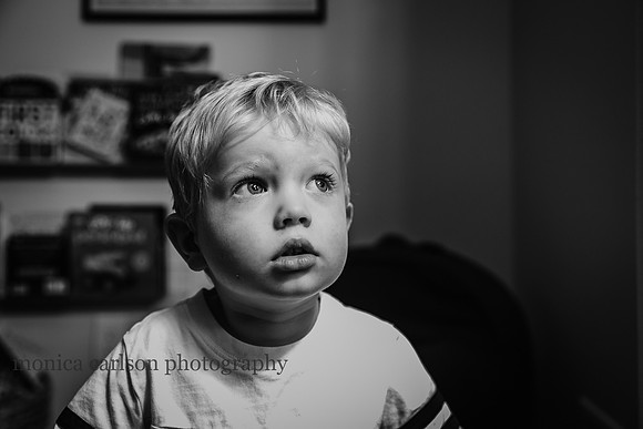 black and white portrait of a little boy looking out a window