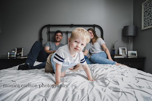 toddler looking at the photographer while his family laughs in the back ground