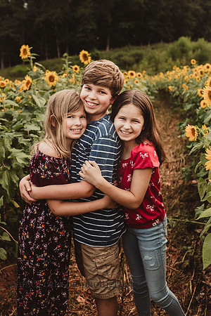 three siblings hug lovingly on a sunflower field at Milford Family Farm
