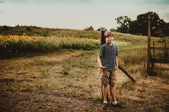 teen boy leans against a fence near a field of flowers
