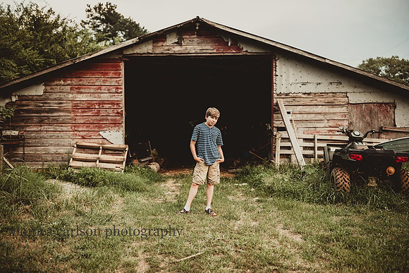 teen boy stand in front of a old barn by monica carlson