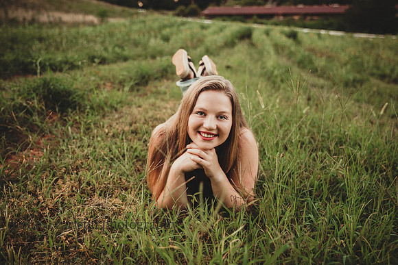 teen girl laying in tall grass during a senior photo session