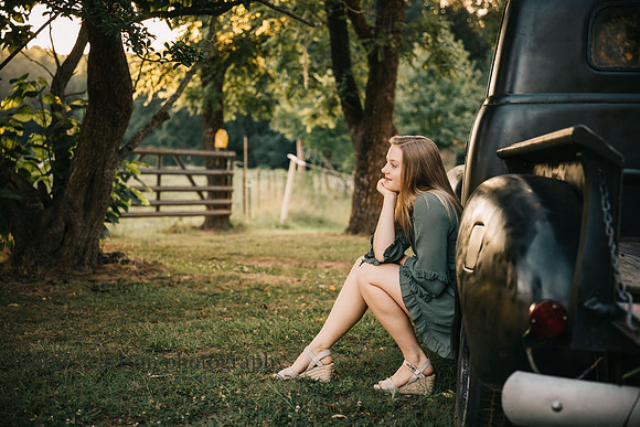 teenager sitting in a tire well of a old truck while looking into the distance