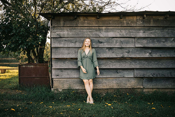 senior girl leaning against a barn during her senior session