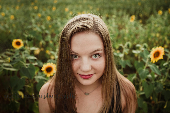 serious portrait of a high school senior in a sunflower field by monica carlson