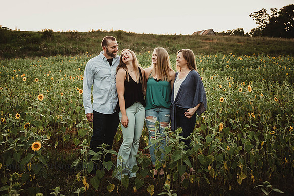 family of four laughing on a sunflower field