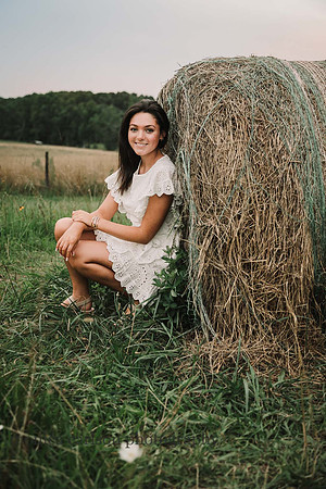 High school senior squats by a huge hay bale at Prospect farms