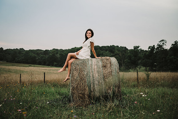 Young woman sits on a hay bale on a farm field in Lawernceville , GA