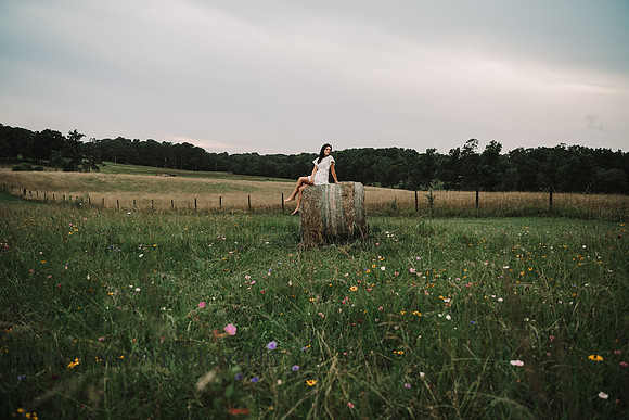 HIgh school senior sits on a hay bale on a flower field by Monica carlson photography