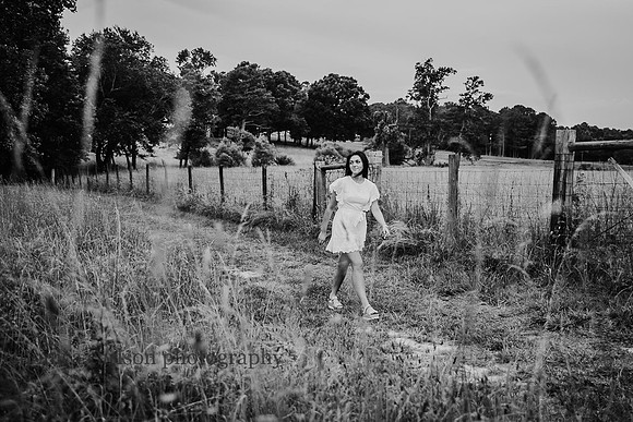 black and white image of a young woman walking along a fence on a farm
