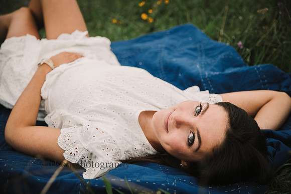 portrait of a young senior laying on her back in a field of flowers by monica carlson