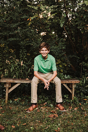 teen boy looking mischieviously while sitting on a bench in roswell, georgia