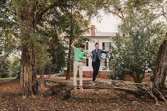 hand holidng siblings jumping from a fallen tree with Bulloch hall in the background