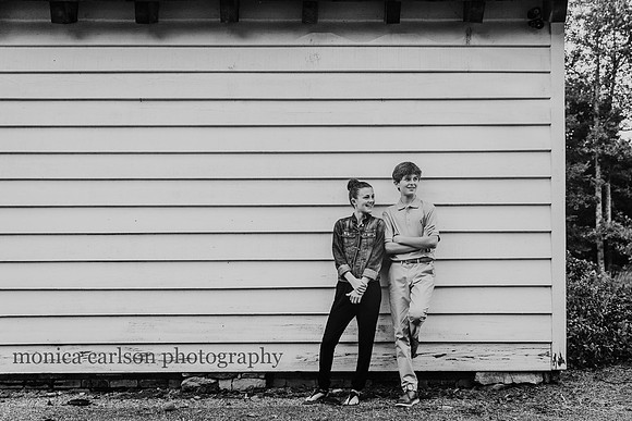 adorable siblings leaning against a barn and looking away