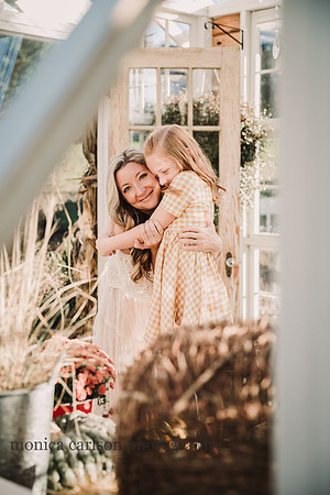 mother hugging her red haired daughter as seen through a greenhouse window