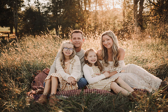 portrait of a family of four in a open field at sunset