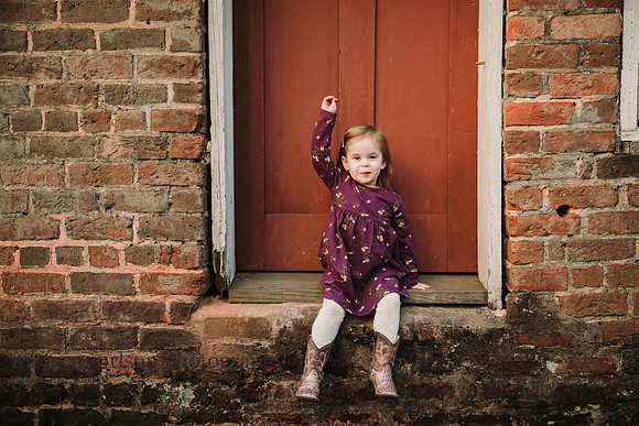 little girl with her arm in the air while sitting in front of a red door of Barrington hall