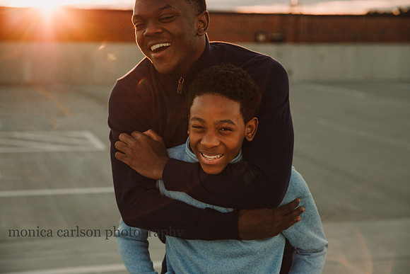 two teen boys embrassing and laughing at sunset in a urban setting by monica carlson photography