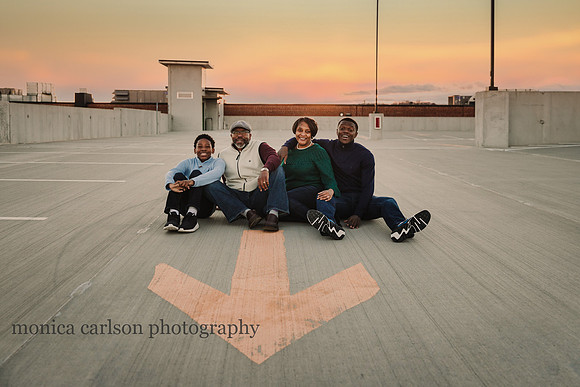 portrait of a happy family siting in a roof top parking lot by monica carlson