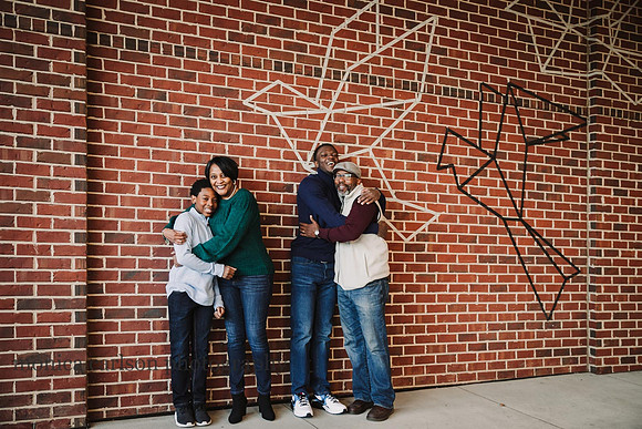 family of four hugging in front of a brick wall that is painted with art