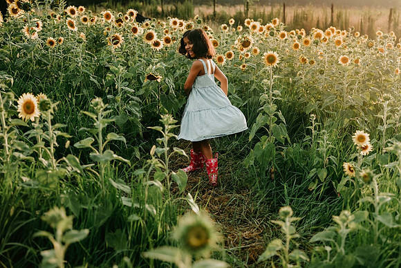 elementary aged girl spinning on a sunflower field while wearing rain boots