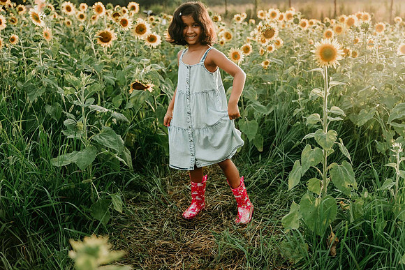 happy elementary aged girl stands among sunflowers by monica carlson