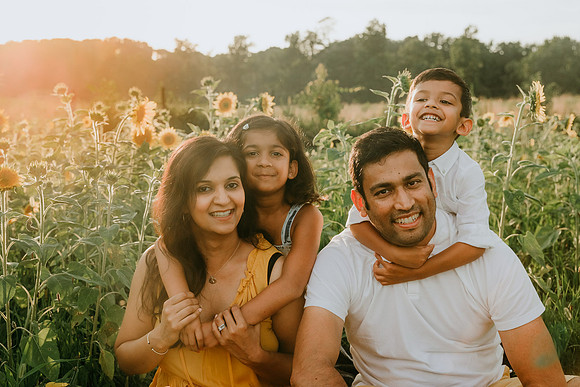 young siblings hugging their parents while sitting in a sunflower field