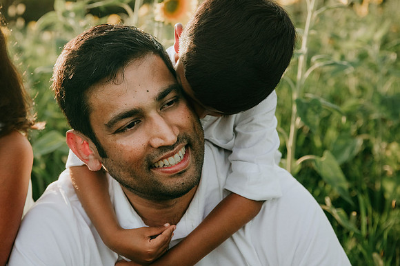 indian father get sneggles from his pre school son from behind during a family photo shoot
